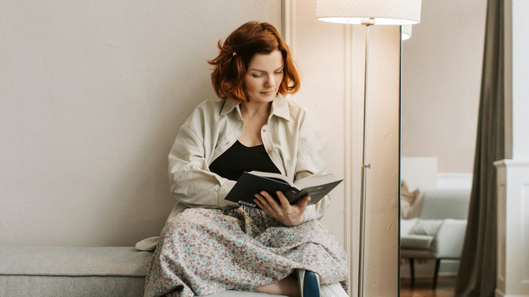 Vrouw leest een boek terwijl ze op de bank zit naast een staande lamp.