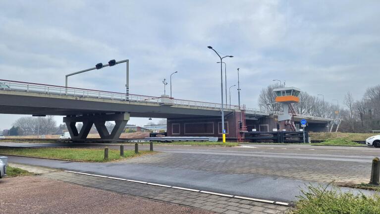 Brug met hefmechanisme en verkeerslichten, naast een grasstrook en een fietspad, onder een bewolkte lucht.