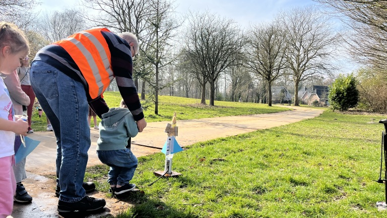 Man en kind lanceren een speelgoedraket in een park.