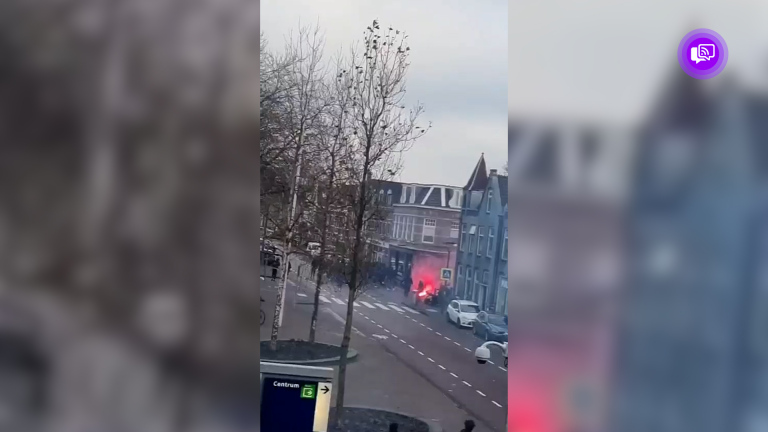 Straatbeeld met rook en vuur, omgeven door bomen en gebouwen.