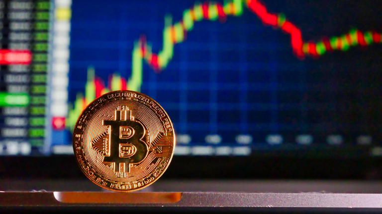 Een Bitcoin-munt voor een scherm met een grafiek van stijgende en dalende koersen.
