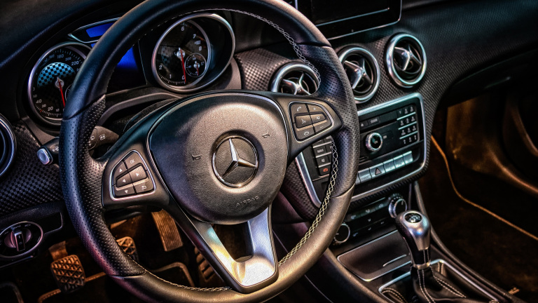 Stuur en dashboard van een Mercedes-Benz met zichtbaar logo, elegante knoppen en klassieke wijzerplaten.