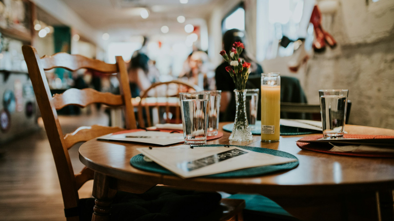 Een gezellig gedekte tafel in een café met glazen water, een brandende kaars, een vaas met bloemen en menukaarten.