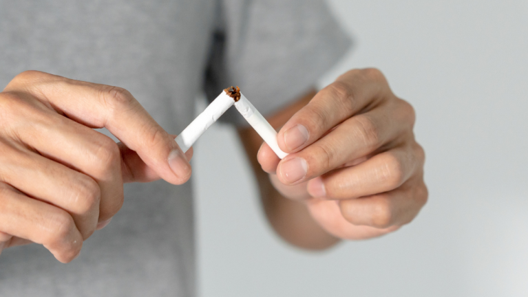 Twee handen breken een sigaret doormidden tegen een neutrale achtergrond.