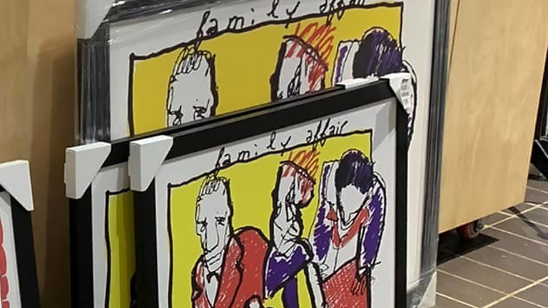 Gestapelde ingelijste kunstwerken met kleurrijke schetsen van figuren en de tekst 'family affair' bovenaan, gepresenteerd in een winkelomgeving.