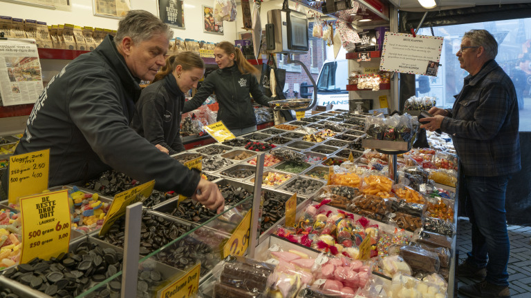 Een marktstal vol met verschillende soorten drop en snoepgoed met klanten die producten bekijken.