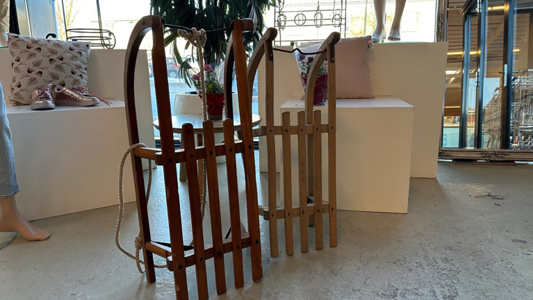 Twee houten sleeën staan in een winkel, omringd door moderne meubelen en decoraties.