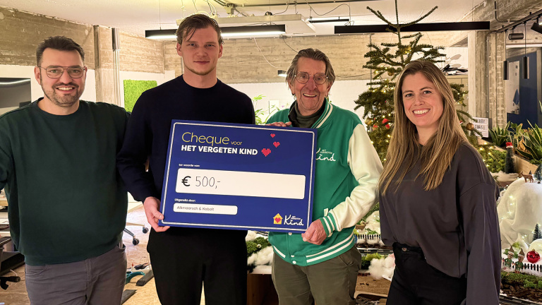 Vier mensen poseren met een cheque van €500 voor "Het Vergeten Kind", met een kerstboom op de achtergrond.