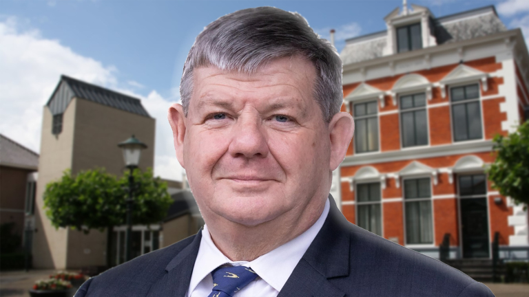 Man in een pak staat voor een gebouw met een rood-witte gevel en klassieke architectuur.