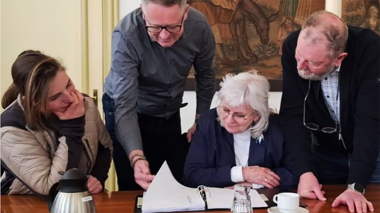 Vier mensen rond een tafel bekijken samen een map met papieren.