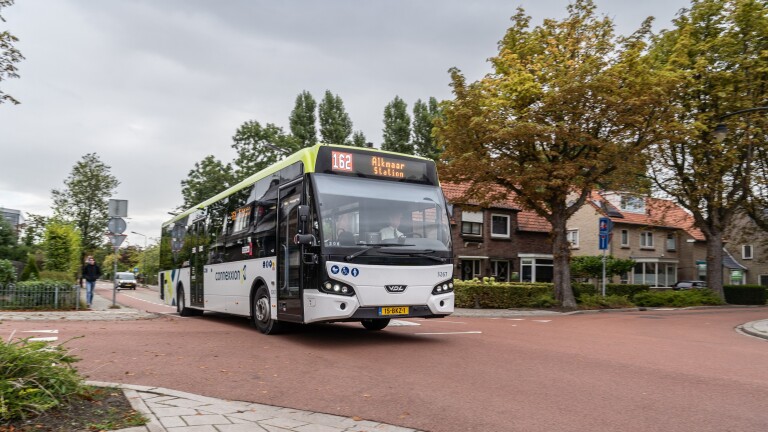 Bus 162 naar Alkmaar Station rijdt door een rustige, met bomen omzoomde straat met huizen op de achtergrond.