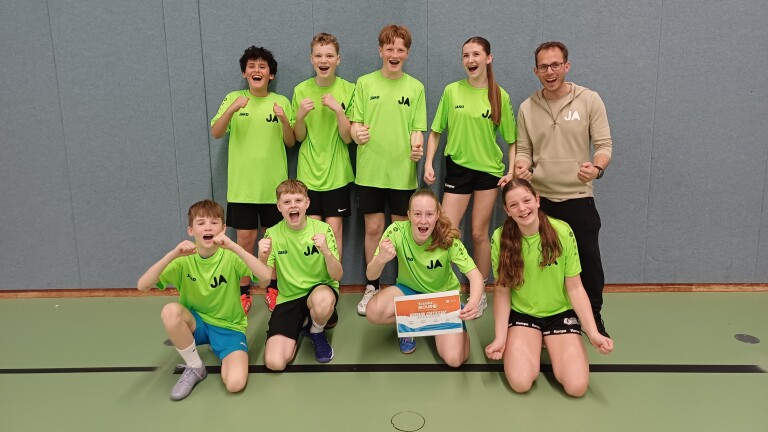 Een enthousiast team van jonge sporters en hun coach poseert in groene shirts in een gymzaal, met een certificaat van deelname.