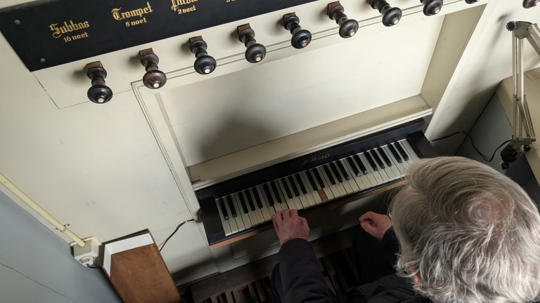 Iemand bespeelt een kerkorgel, met een rij registerknoppen en zichtbare toetsen.