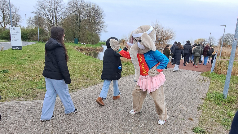 Een persoon in een konijnenpak met een rode sjerp geeft high-fives aan voorbijgangers op een wandelpad.