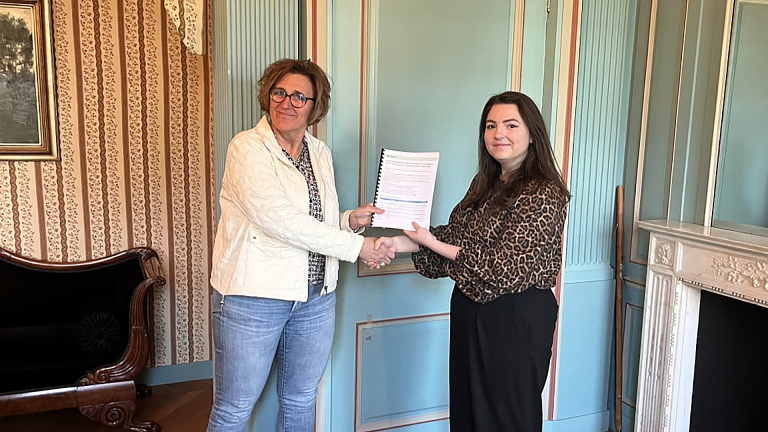 Twee vrouwen schudden elkaar de hand terwijl ze samen een document vasthouden in een elegant ingerichte kamer.