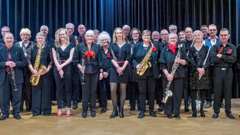 Een groep muzikanten poseert met hun instrumenten op een podium; sommigen dragen rode accenten.