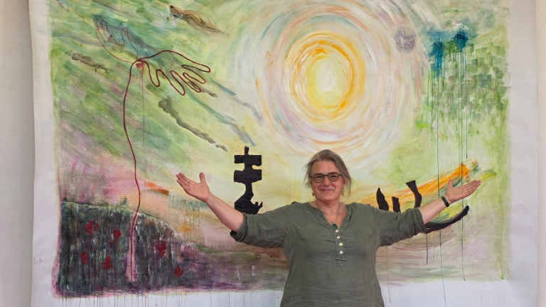 Vrouw staat met uitgestrekte armen voor kleurrijk schilderij met zon en abstracte vormen.