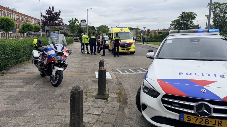 Politie- en ambulancevoertuigen verzamelen zich langs de weg, met agenten en ambulancepersoneel die met elkaar praten.