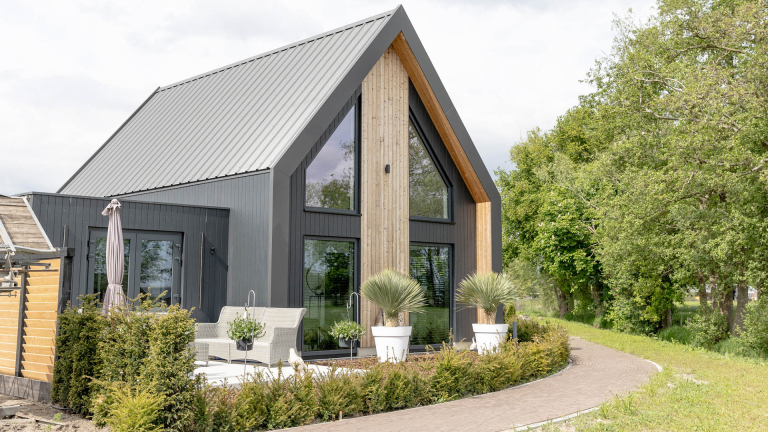 Modern huis met een zadeldak, grote ramen en houten gevelbekleding, omgeven door een tuin met planten en een terras.