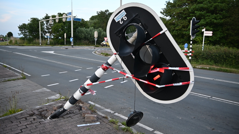 Een omgewaaide verkeerslichtenpaal ligt over een stoep, omringd door rood-wit waarschuwingslint.