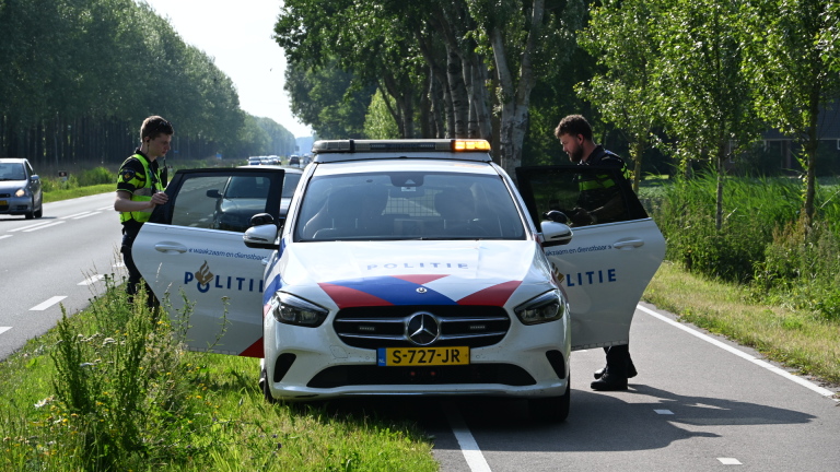 Politiewagen met zwaailichten aan en twee agenten staan bij de geopende voordeuren, langs een landelijke weg omringd door bomen.