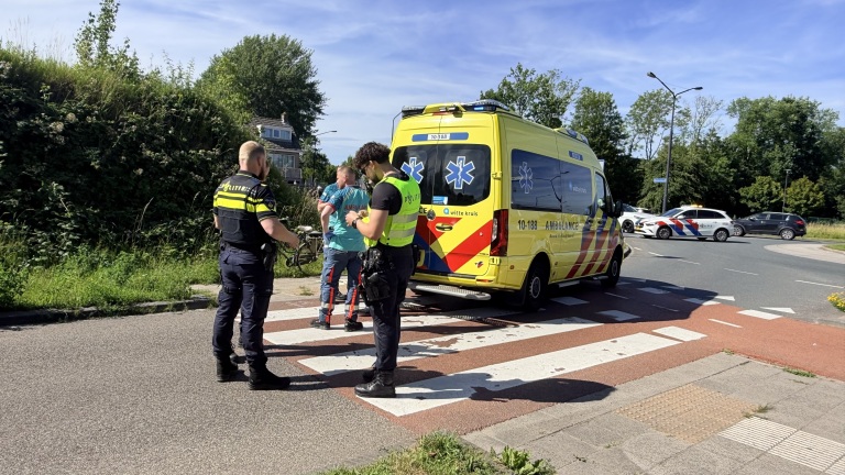 Politieagenten en ambulancepersoneel bij een gele ambulance op een kruispunt.