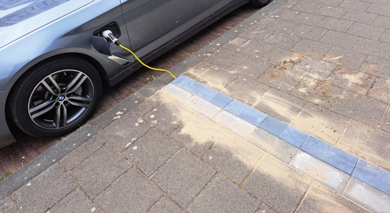 Elektrische auto is aangesloten op een oplaadkabel, geparkeerd langs de stoep met een oplaadpunt dat in de grond is geïntegreerd.