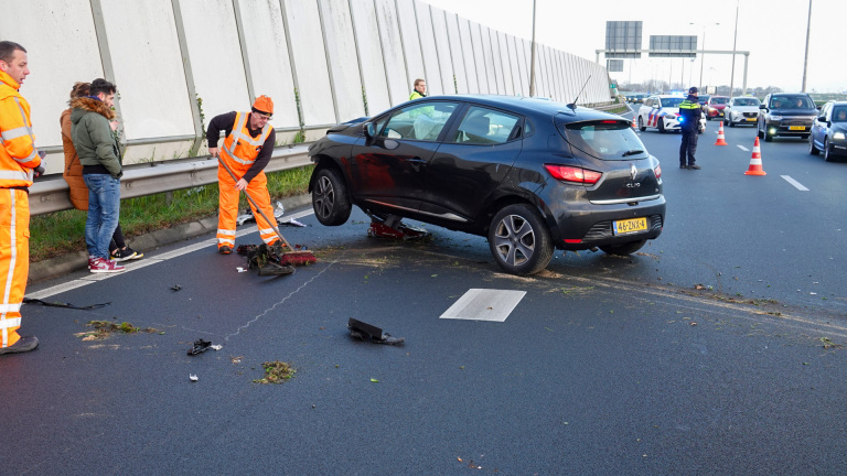 Auto met zware schade aan de voorkant na een verkeersongeval, met sleepwagen en omstanders op de achtergrond.