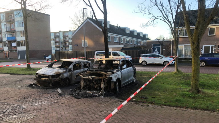 Twee verbrande auto's staan in een parkeerplaats, omringd door rood-wit lint in een woonwijk.