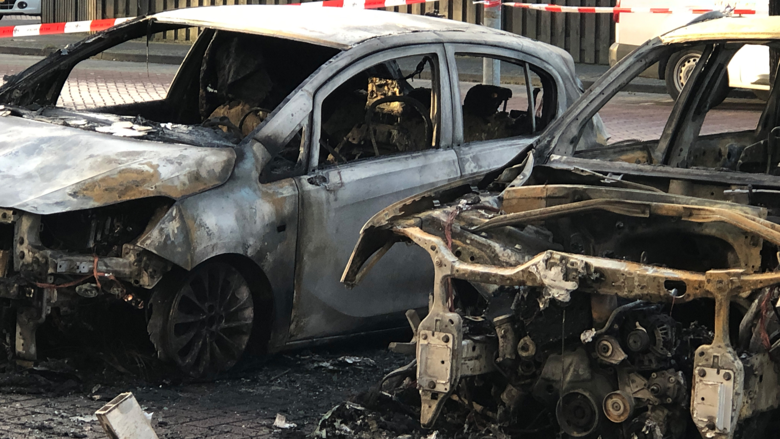 Twee verbrande auto's staan in een parkeerplaats, omringd door rood-wit lint in een woonwijk.