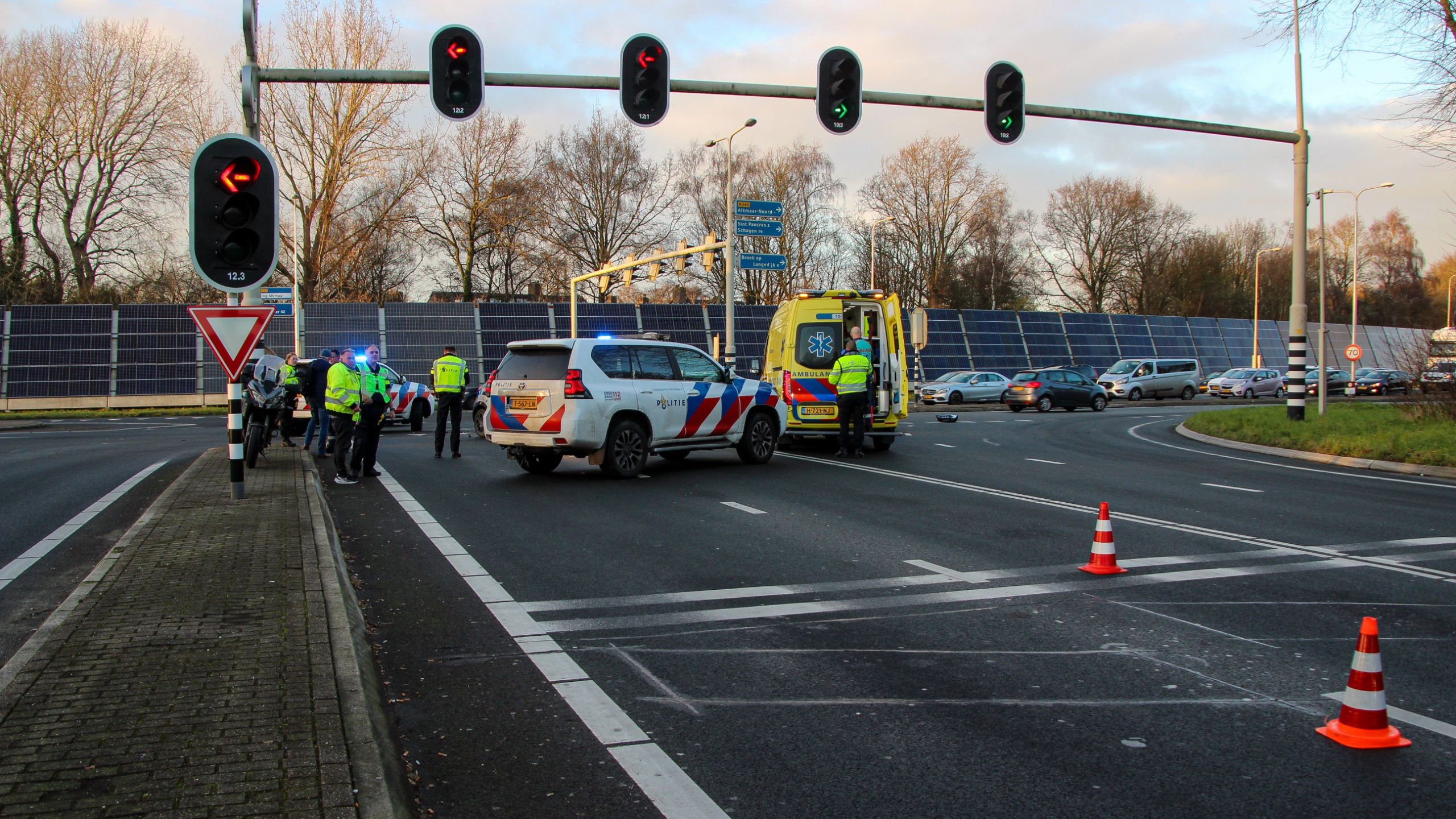 Politie- en ambulances staan bij een kruispunt met verkeerslicht; mensen in uniform overleggen.