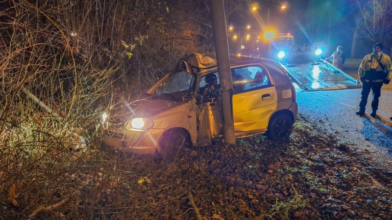 Auto botst tegen boom langs weg bij nacht, met een bergingsvoertuig en hulpverlener aanwezig.