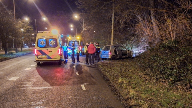 Auto botst tegen boom langs weg bij nacht, met een bergingsvoertuig en hulpverlener aanwezig.