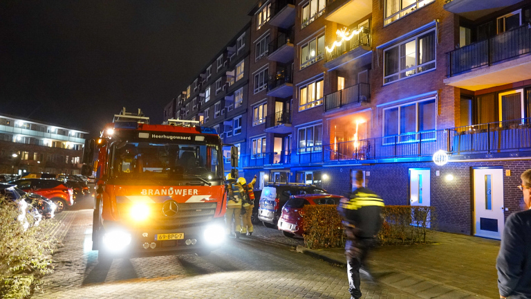 Brand op een balkon van een appartementencomplex, met vlammen zichtbaar rond de deur, naast gesloten ramen.