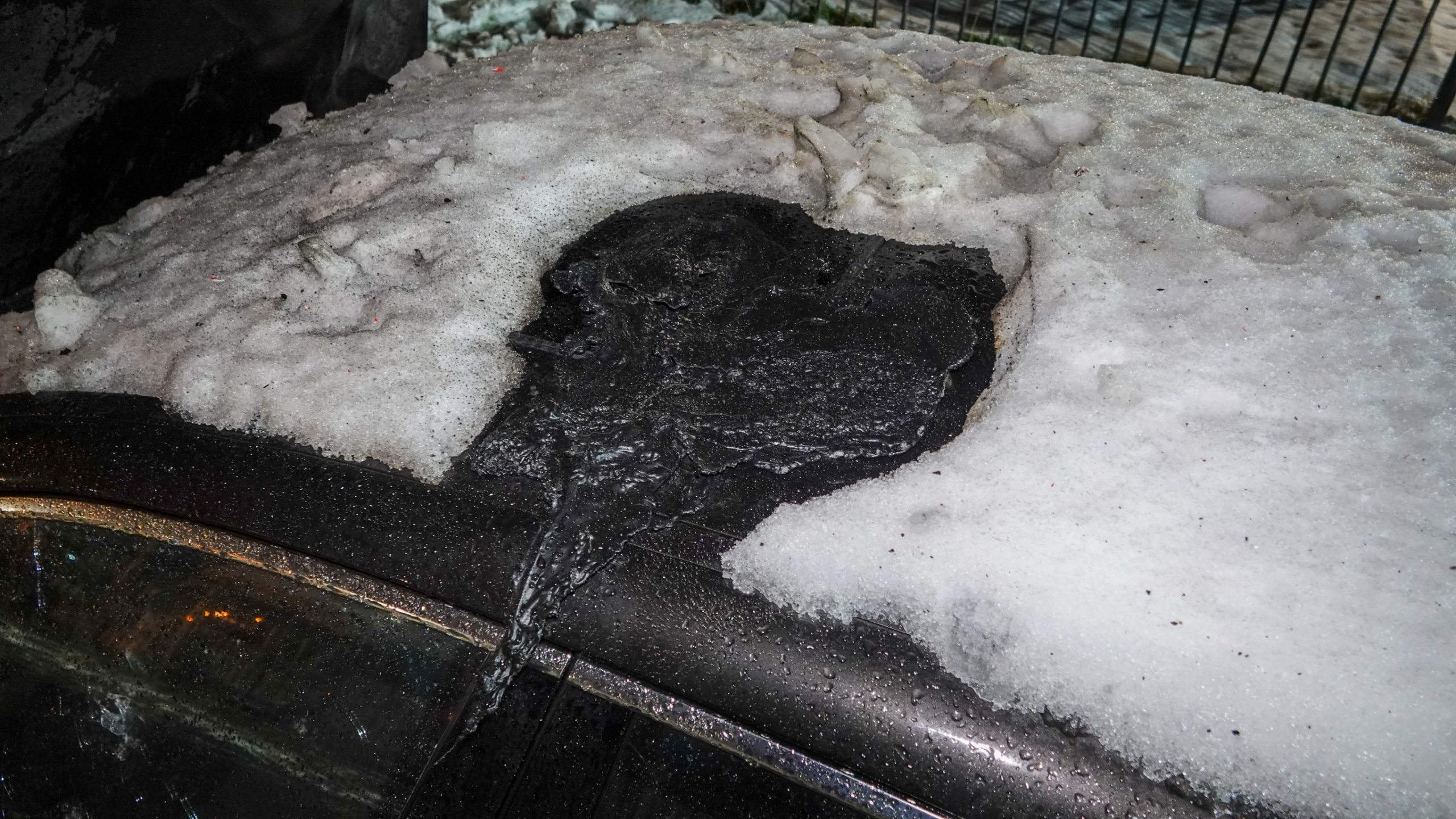 Brandweerlieden blussen 's nachts een brand in een zwarte auto, omringd door schuim en water op de grond.