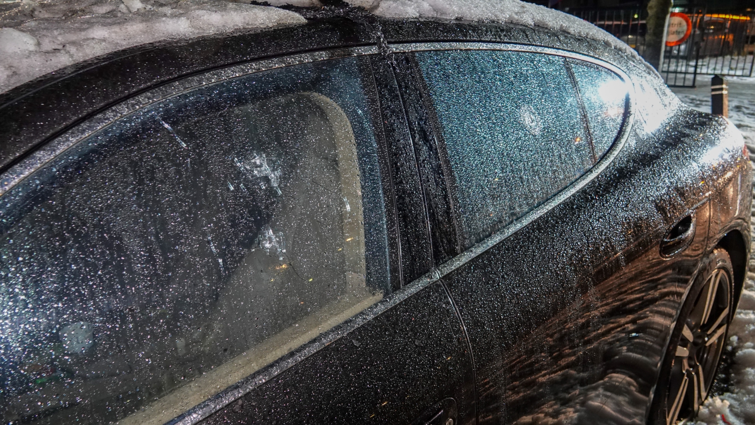 Brandweerlieden blussen 's nachts een brand in een zwarte auto, omringd door schuim en water op de grond.