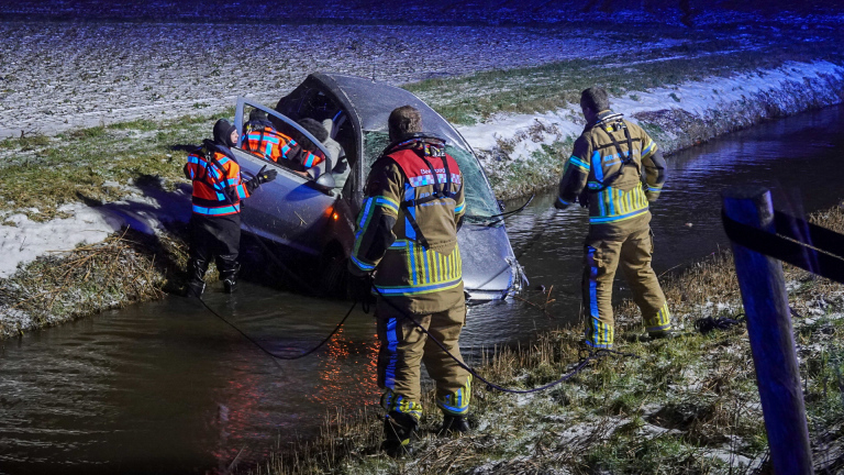 Brandweerlieden redden mensen uit een auto die scheef in een besneeuwde sloot ligt.