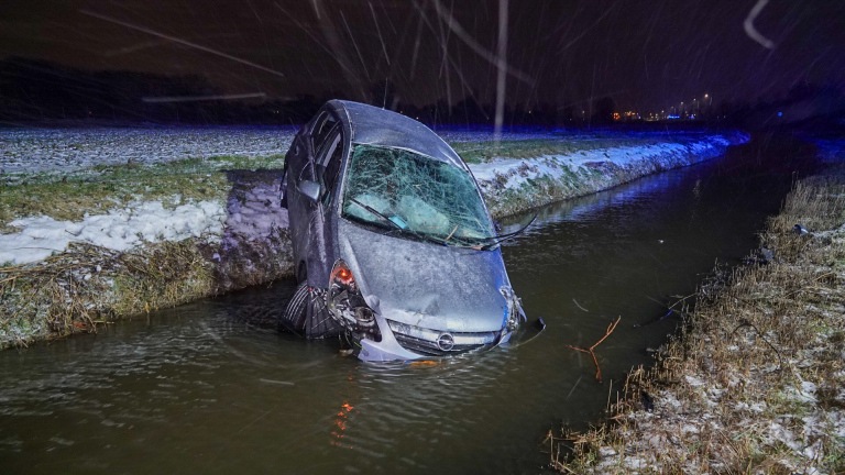 Brandweerlieden redden mensen uit een auto die scheef in een besneeuwde sloot ligt.
