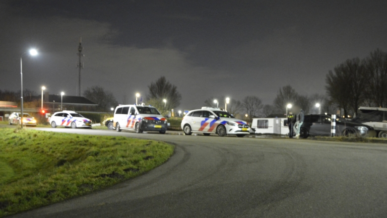Meerdere politieauto's staan geparkeerd langs een weg in de nacht, met agenten bij een voertuig.
