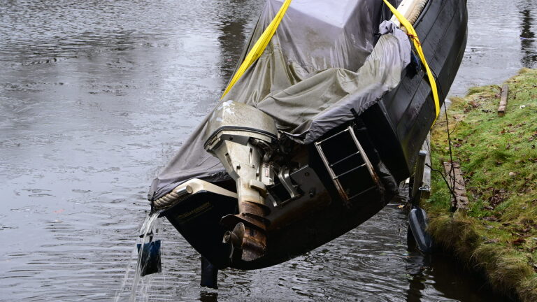 Brandweerlieden en een duiker halen een auto uit het water met behulp van een kraan langs een oever.