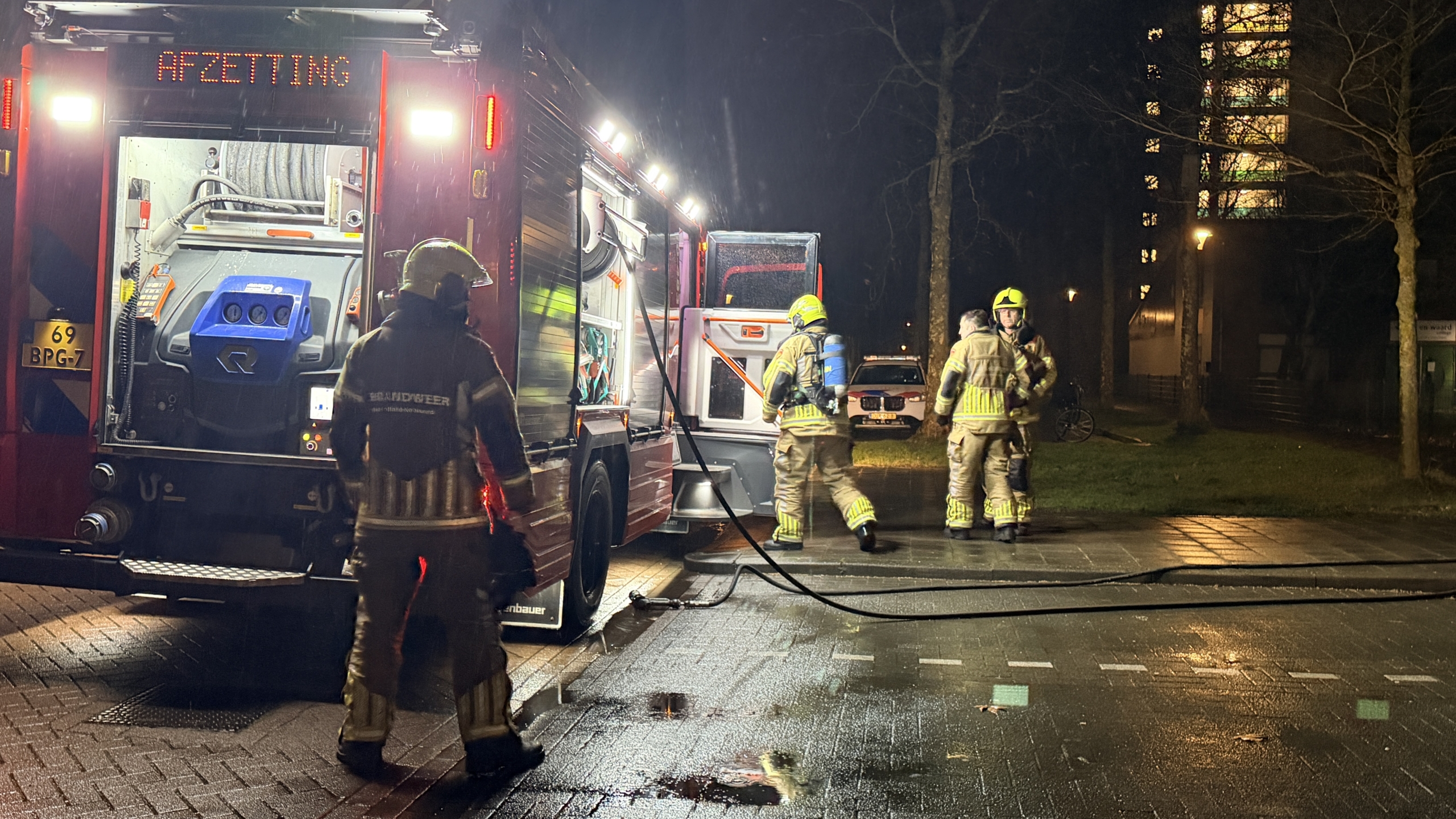 Brandweerman blust brandende scooter langs een pad, omgeven door rook en bomen.