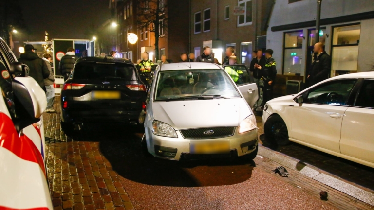 Drie auto's zijn betrokken bij een botsing op een natte straat, met een politieauto en agenten op de achtergrond.