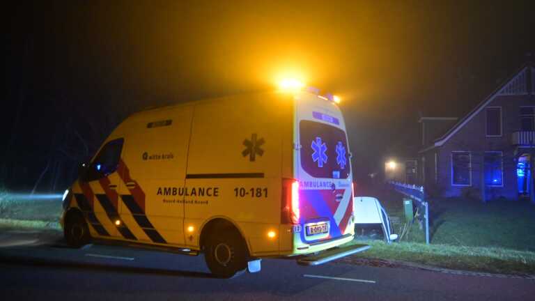 Witte auto rijdt in een sloot bij nacht; politieman en persoon staan bij een stenen muur met de tekst "VEILIGST."