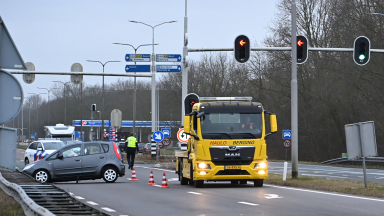Auto met schade aan de voorzijde naast een vangrail op de snelweg, met een gele sleepwagen op de achtergrond.