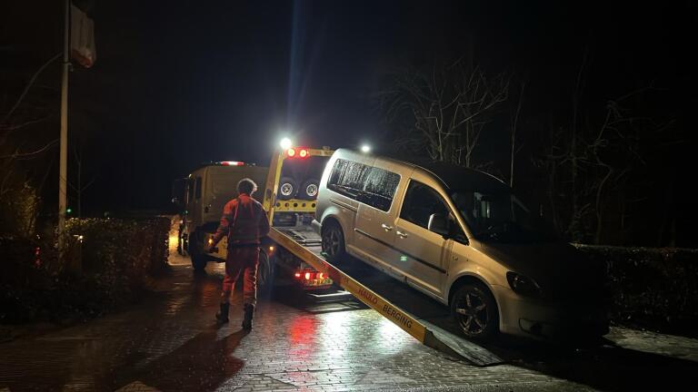Politieagent met hond onderzoekt een donkere weg waar een auto op zijn zij ligt naast de weg.