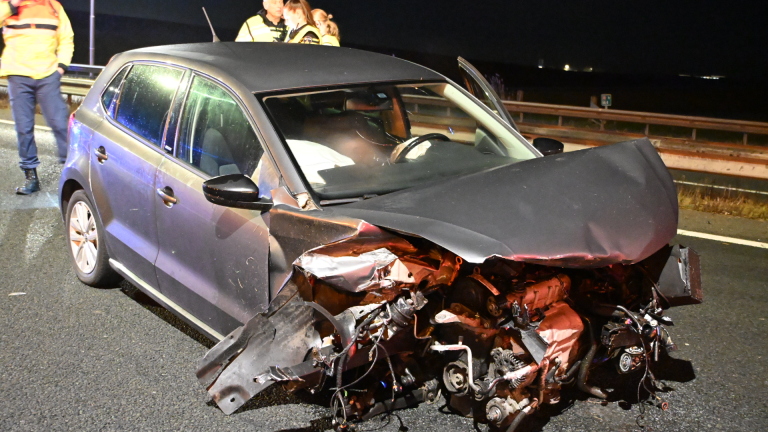 Politievoertuig met zwaailichten blokkeert een snelweg na een ongeval; meerdere auto's en agenten in actie.