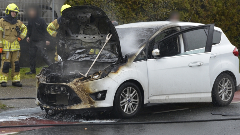 Brandweerlieden blussen een motorbrand van een beschadigde auto met brandweeruitrusting en -slangen.