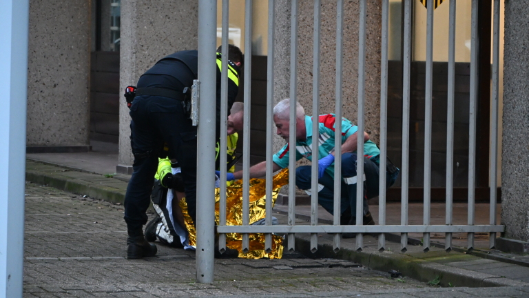 Politieagent en twee ambulances voor een flatgebouw met een politievoertuig op de achtergrond.