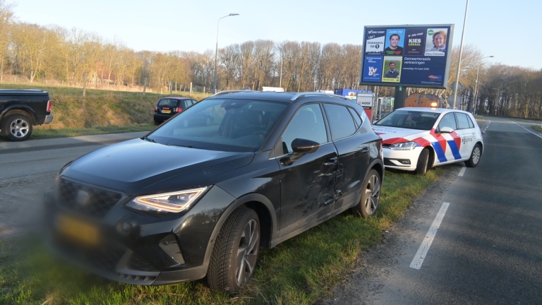 Politieagenten staan naast meerdere politievoertuigen langs de weg, met een groot verkiezingsbord op de achtergrond.
