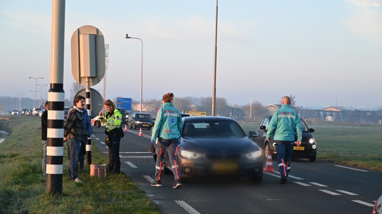 Auto-ongeluk met een ambulance en hulpverleners op de weg, waarbij meerdere auto's en verkeersborden zichtbaar zijn.